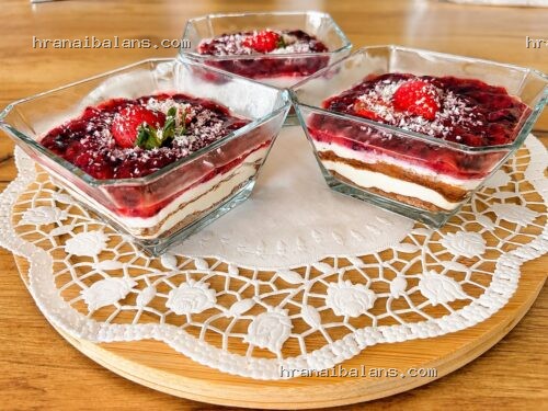 Four square glass bowls on a lace doily each with layered berry sauce cream and biscuit crumbs on a wooden table